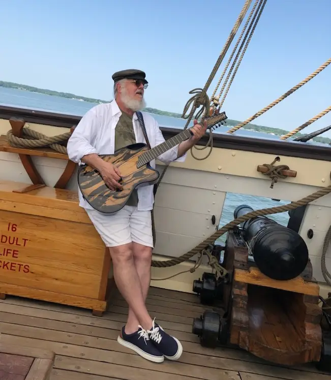 Man-enjoying-playing-his-emerald-guitar-on-a-sail-boat-in-sunny-climate