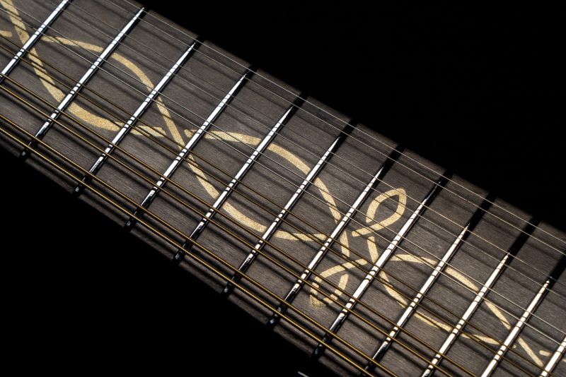 Close-up of guitar fretboard with detailed Celtic vine inlays and nickel frets